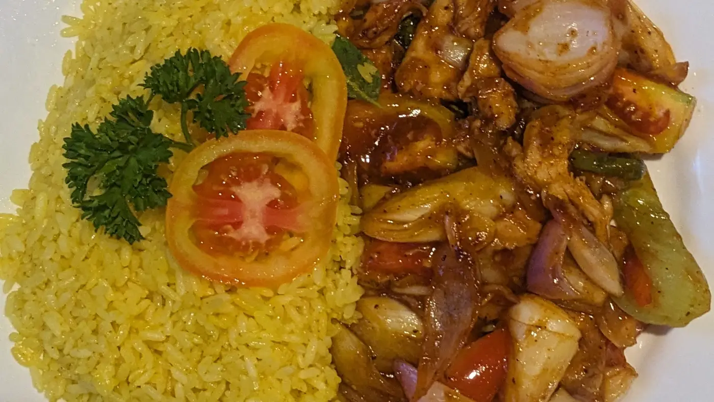 A plate of yellow rice with devilled chicken, peppers and onions