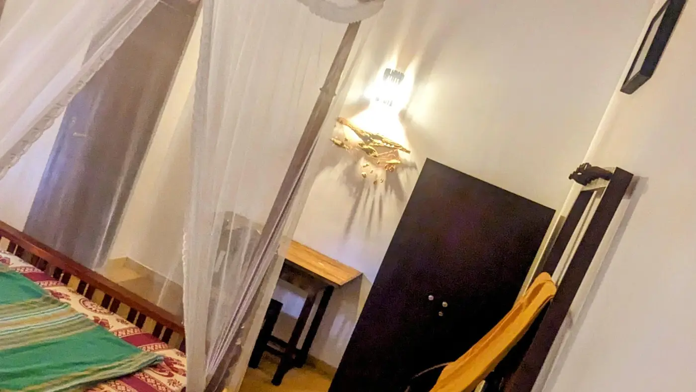 A deluxe room at Surfing Life with a four-poster bed, mosquito net and ceiling fan